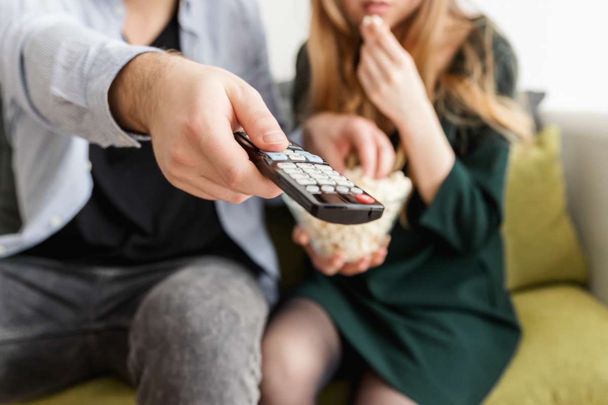 Un uomo e una donna seduti sul divano. Lui ha il telecomando in mano