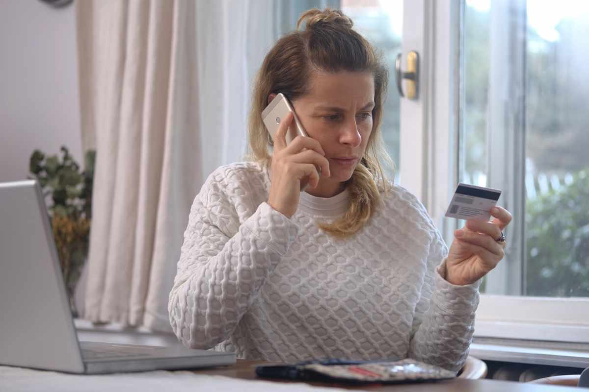 Donna che guarda carta di credito con cellulare all'orecchio