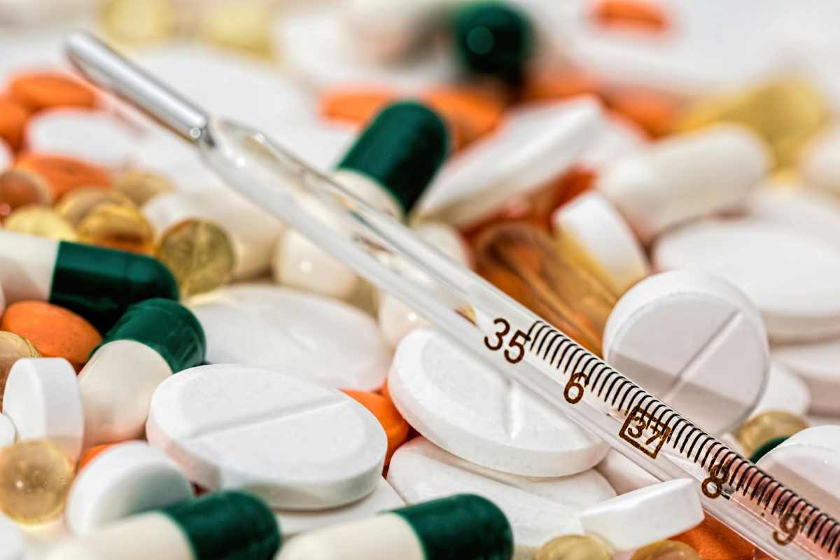 Pillole e pasticche mediche ammucchiate, con un termometro al mercurio